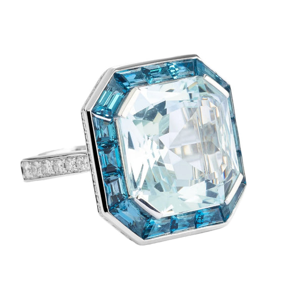 Bague pour femme en or blanc pavée de diamants blancs avec un solitaire d'aigue-marine entouré de topazes bleues. Bague Michaud 143790